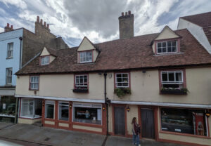 A two-story cream-colored building with a tiled roof, three dormer windows, and a ground-floor restaurant storefront.