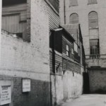 A narrow alleyway with weatherboarded buildings and a brick wall featuring a Post Office private no parking sign.