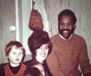 A smiling man and woman sit behind three young children and a baby in a room with wood-paneled walls in November 1971.