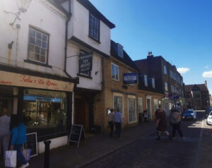 A street scene in Ely showing historic shop fronts, including Julia’s Tea Rooms, with pedestrians walking along the pavement.