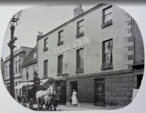 A horse-drawn carriage stands outside the three-story Bell Inn, with a woman in a long dress standing in the doorway.